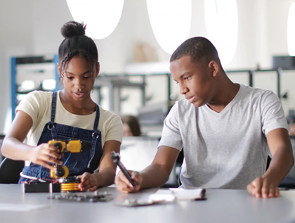 Image of two black students (one girl and one boy) happily constructing a robotic arm